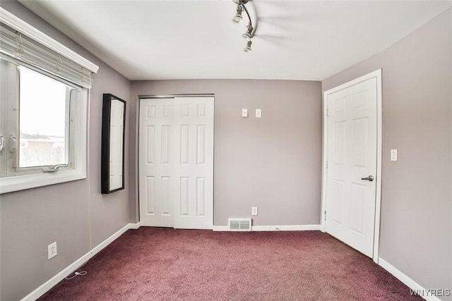 unfurnished bedroom with dark carpet, track lighting, and a closet