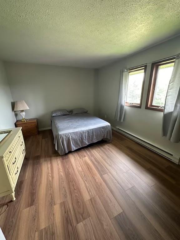 unfurnished bedroom featuring a baseboard heating unit, dark wood-type flooring, and a textured ceiling