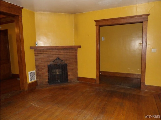 unfurnished living room featuring hardwood / wood-style flooring and a brick fireplace