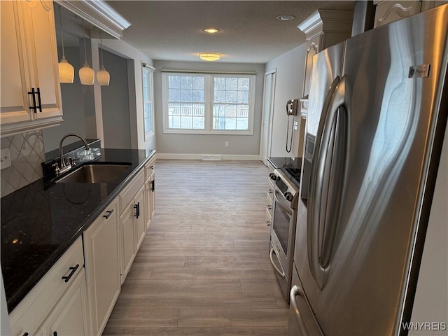 kitchen with pendant lighting, sink, appliances with stainless steel finishes, dark stone counters, and light wood-type flooring