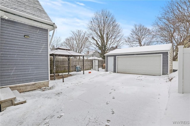 snowy yard featuring a garage, a gazebo, and an outdoor structure