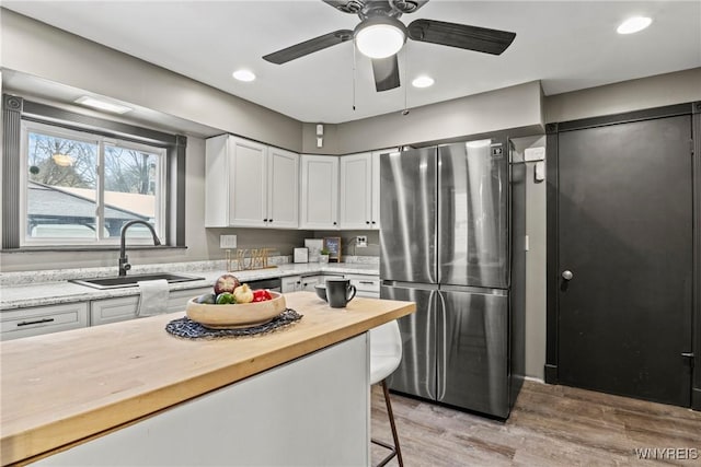 kitchen with butcher block countertops, white cabinetry, sink, stainless steel fridge, and a kitchen bar