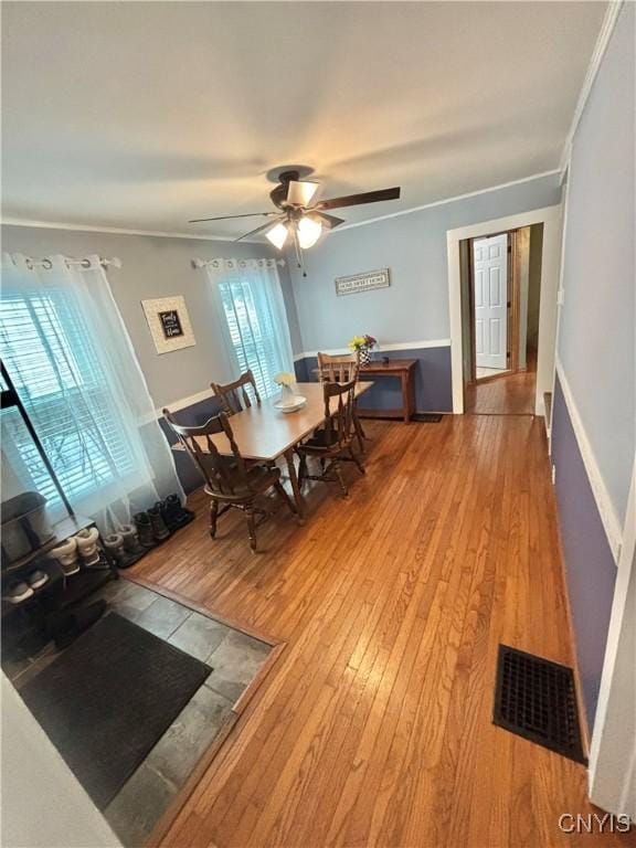 dining area with wood-type flooring, ornamental molding, and ceiling fan