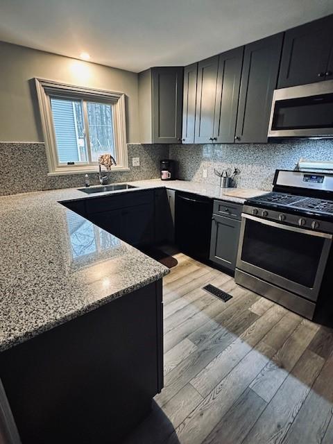 kitchen featuring light wood-type flooring, stainless steel appliances, light stone countertops, sink, and tasteful backsplash