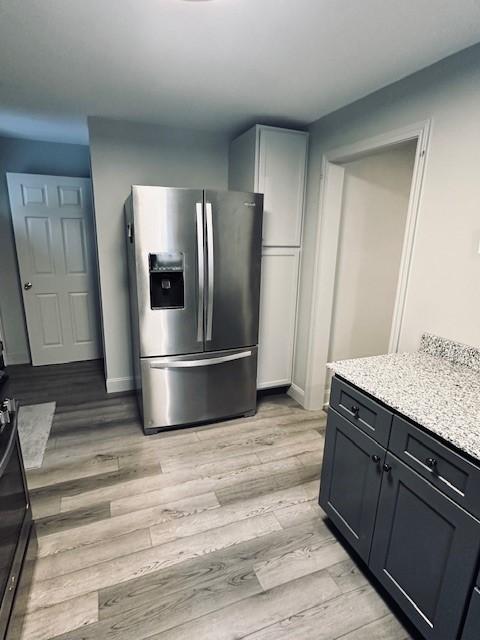 kitchen with light wood-type flooring, light stone counters, and stainless steel refrigerator with ice dispenser