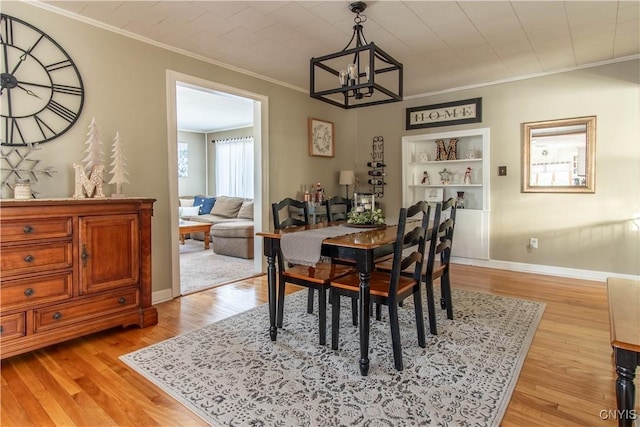 dining space featuring a notable chandelier, light hardwood / wood-style flooring, built in features, and ornamental molding