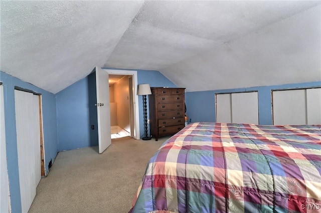 unfurnished bedroom featuring two closets, vaulted ceiling, light carpet, and a textured ceiling