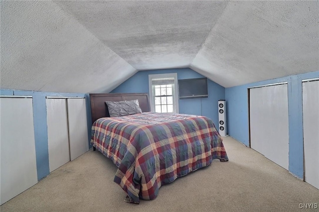 carpeted bedroom featuring lofted ceiling, a textured ceiling, and two closets