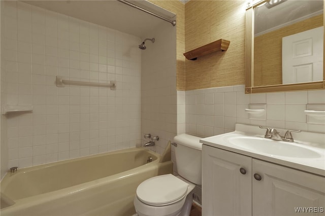 full bathroom with tile walls, tiled shower / bath combo, vanity, and toilet