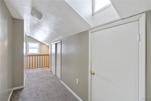 hallway featuring carpet, lofted ceiling, and a textured ceiling