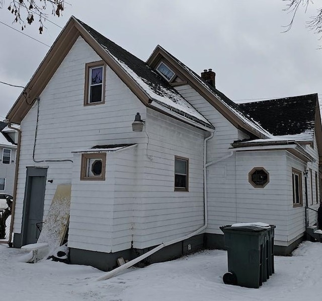 snow covered rear of property with a chimney