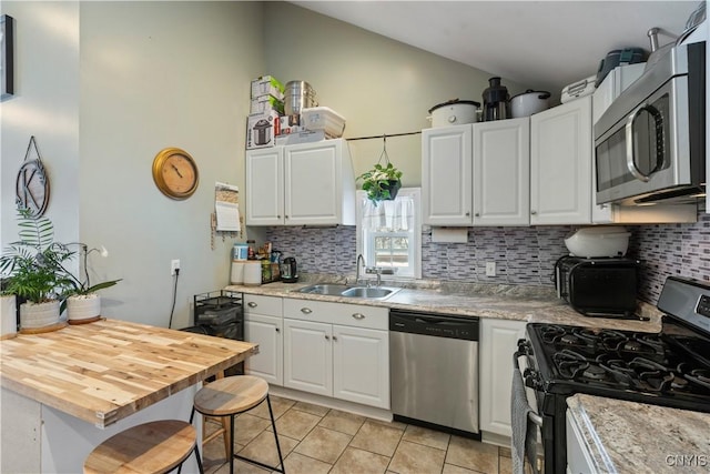 kitchen featuring lofted ceiling, a breakfast bar, sink, appliances with stainless steel finishes, and white cabinets