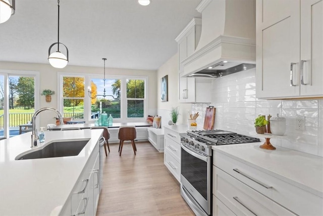 kitchen featuring sink, custom exhaust hood, decorative light fixtures, stainless steel range with gas cooktop, and white cabinets