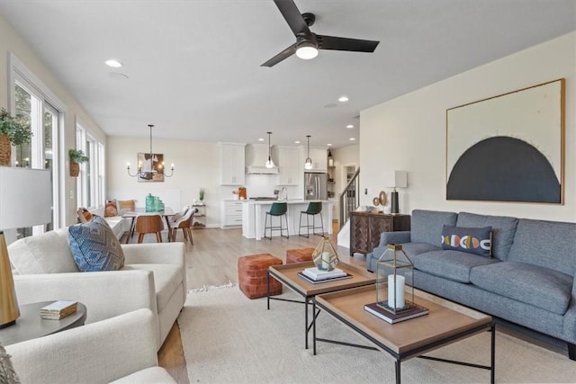 living room featuring ceiling fan with notable chandelier and light hardwood / wood-style flooring