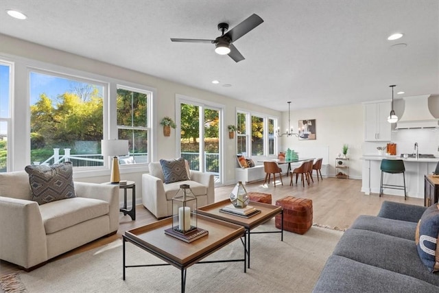 living room featuring ceiling fan with notable chandelier, light wood-type flooring, and sink