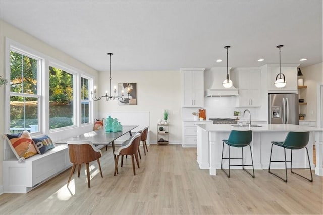 kitchen featuring sink, custom exhaust hood, white cabinetry, decorative light fixtures, and stainless steel fridge