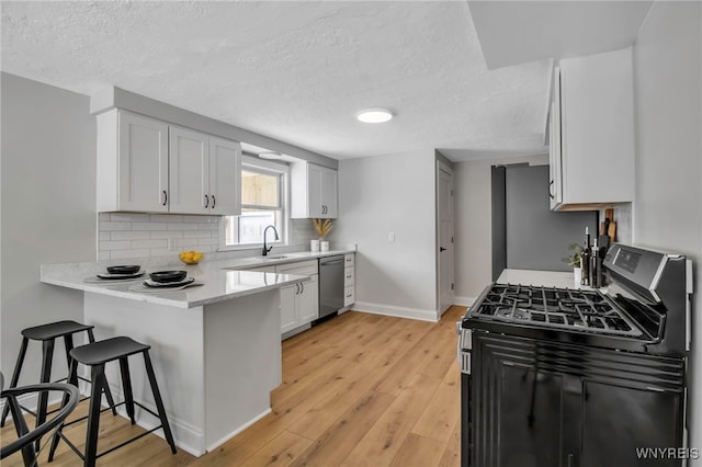 kitchen featuring stainless steel appliances, light hardwood / wood-style floors, tasteful backsplash, white cabinets, and a kitchen breakfast bar