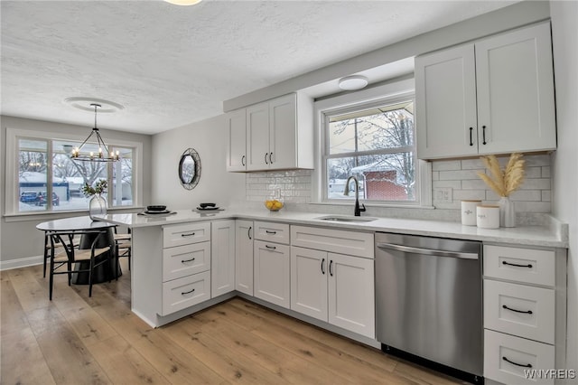 kitchen featuring light wood-type flooring, white cabinetry, hanging light fixtures, sink, and dishwasher