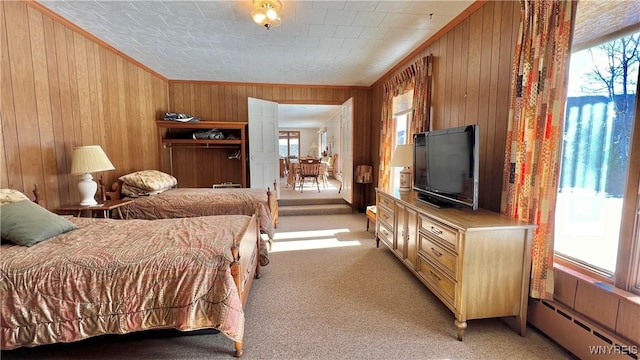 carpeted bedroom with a baseboard heating unit, ornamental molding, multiple windows, and wooden walls