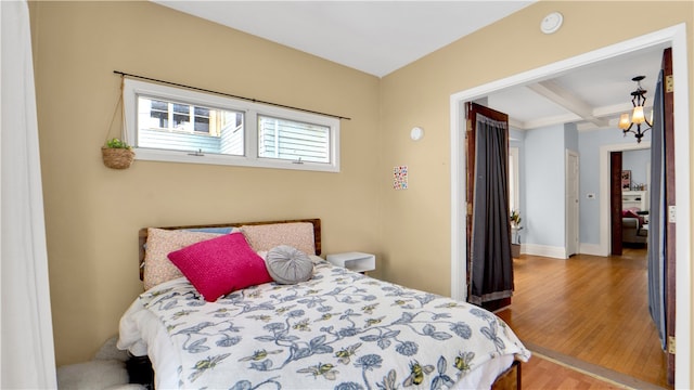 bedroom featuring hardwood / wood-style flooring, beamed ceiling, a chandelier, and coffered ceiling