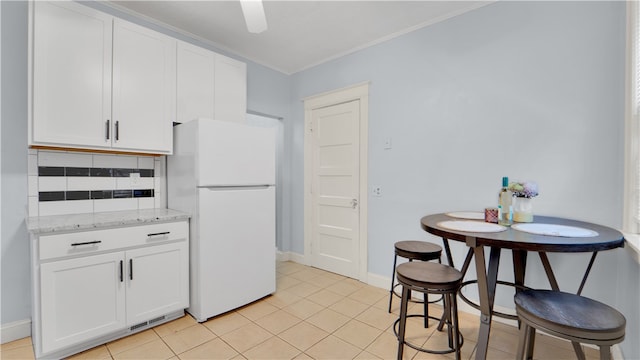 kitchen with tasteful backsplash, white cabinetry, white refrigerator, and light stone counters