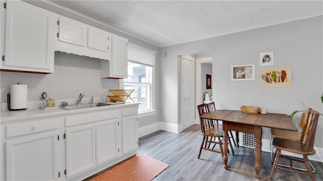 kitchen featuring ornamental molding, light hardwood / wood-style flooring, sink, and white cabinets