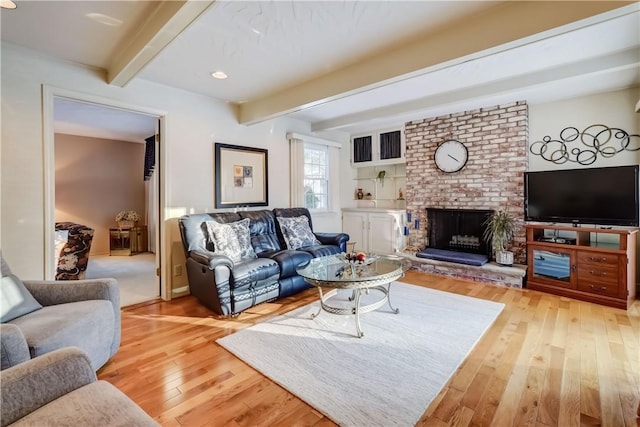 living room featuring a fireplace, beamed ceiling, and light hardwood / wood-style floors