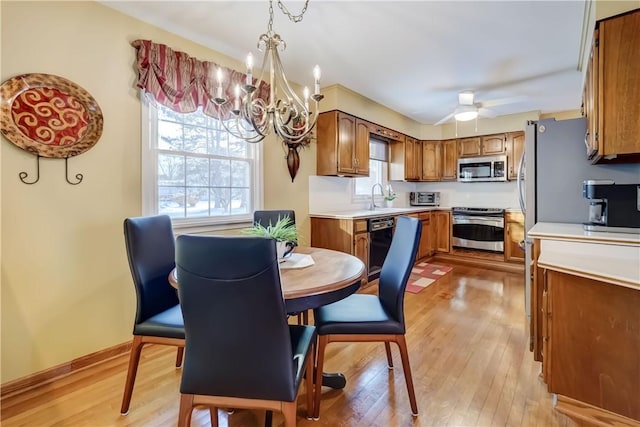 dining area with sink, light wood-type flooring, and ceiling fan with notable chandelier