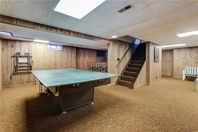 recreation room featuring a drop ceiling, carpet floors, and wood walls