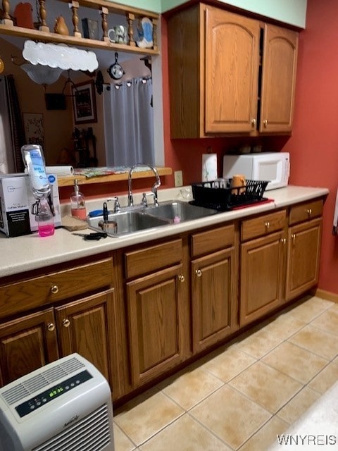 kitchen featuring brown cabinetry, light tile patterned flooring, white microwave, and a sink