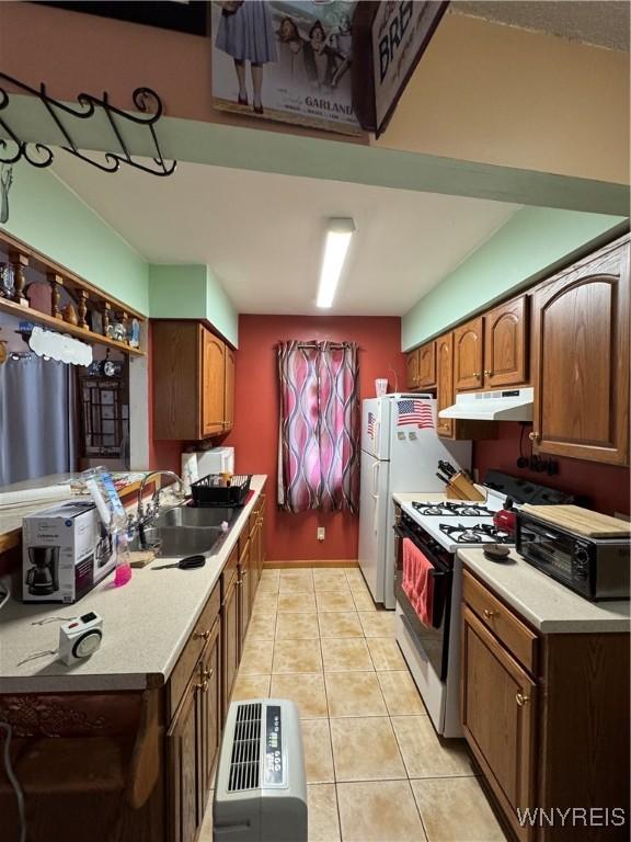 kitchen featuring range with gas cooktop, under cabinet range hood, light countertops, light tile patterned floors, and a sink