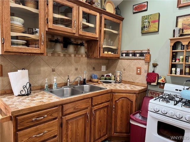 kitchen with a sink, backsplash, brown cabinetry, and white gas range oven