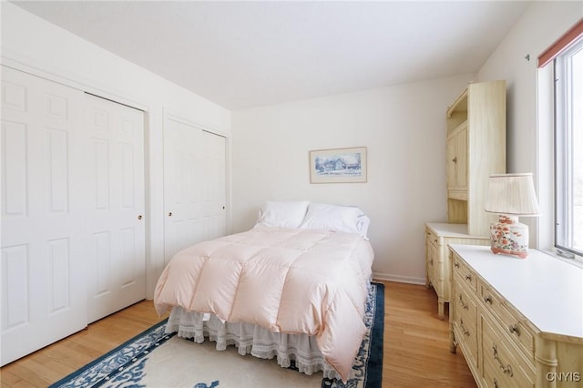 bedroom with multiple windows, light wood-type flooring, and two closets