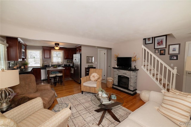 living room featuring a fireplace, sink, light hardwood / wood-style floors, and ceiling fan