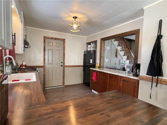 kitchen with black refrigerator, light stone counters, dark wood-type flooring, crown molding, and sink