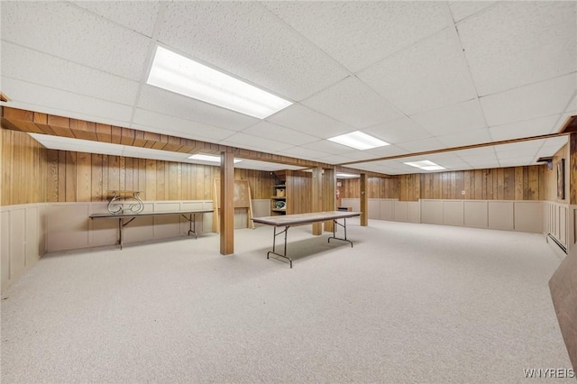 basement with a paneled ceiling, wooden walls, and carpet flooring