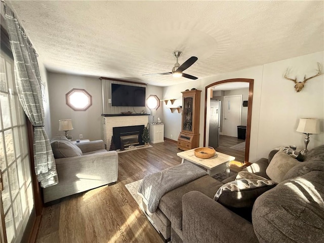 living room with a textured ceiling, dark wood-type flooring, ceiling fan, and a fireplace