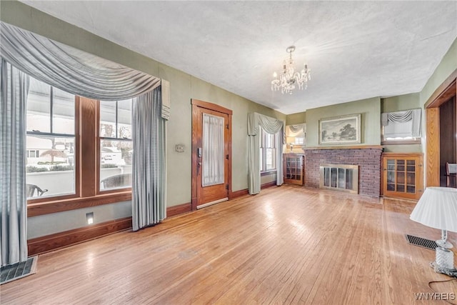 unfurnished living room with hardwood / wood-style floors, a chandelier, and a brick fireplace