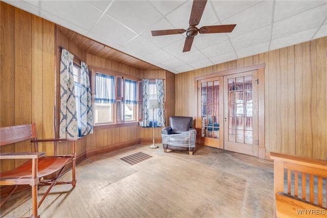 living area with a paneled ceiling, french doors, ceiling fan, wood walls, and hardwood / wood-style floors