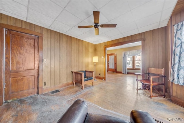 interior space with ceiling fan, wooden walls, and a paneled ceiling