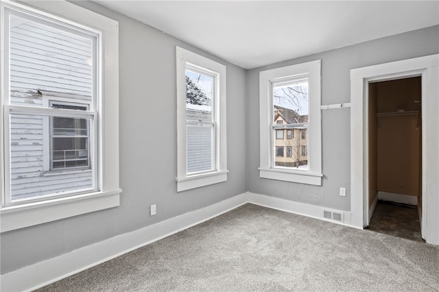 unfurnished bedroom with carpet floors, a walk in closet, a closet, visible vents, and baseboards