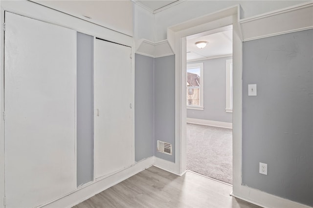 interior space with light carpet, visible vents, baseboards, ornamental molding, and light wood-type flooring