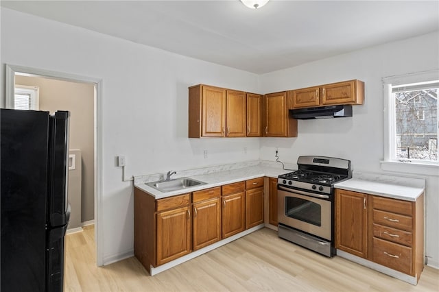 kitchen featuring freestanding refrigerator, stainless steel gas range, light countertops, under cabinet range hood, and a sink