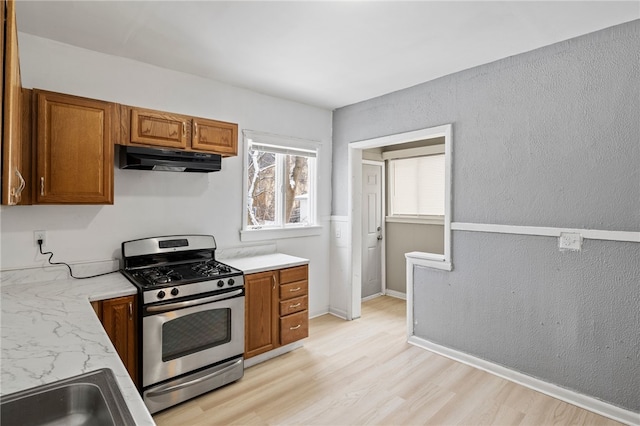 kitchen with stainless steel gas stove, light wood-style flooring, brown cabinets, light countertops, and under cabinet range hood