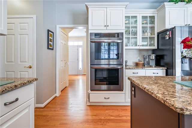 kitchen with white cabinetry, stainless steel appliances, light hardwood / wood-style flooring, tasteful backsplash, and light stone counters