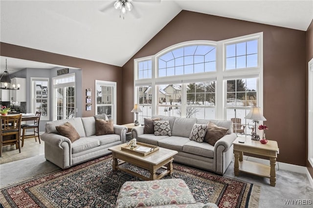 carpeted living room with ceiling fan with notable chandelier and high vaulted ceiling