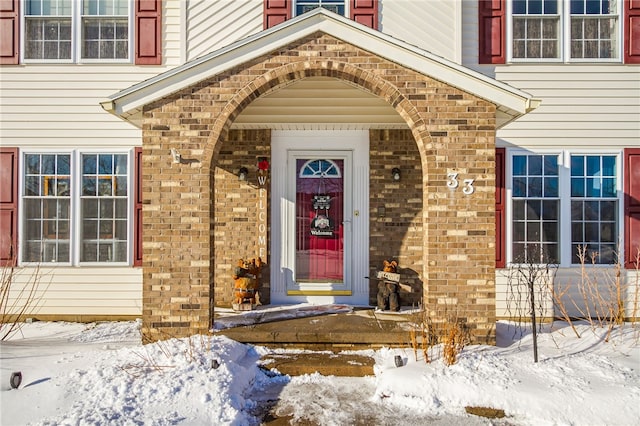 snow covered property entrance featuring brick siding