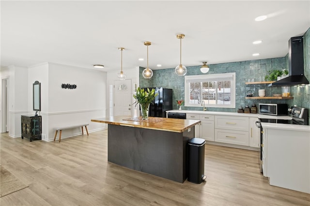 kitchen featuring wall chimney exhaust hood, black appliances, pendant lighting, a kitchen island, and white cabinetry