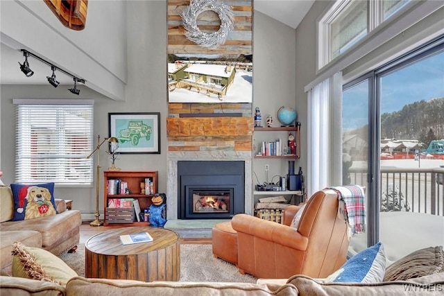 living room featuring track lighting, high vaulted ceiling, a baseboard radiator, and a fireplace