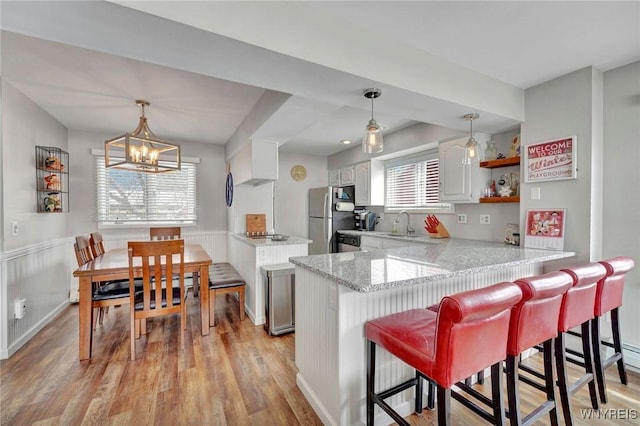 kitchen with stainless steel refrigerator, light wood-type flooring, white cabinetry, a kitchen bar, and kitchen peninsula